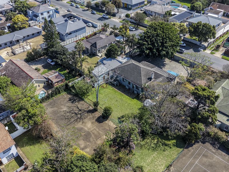 Aerial view of the property showcasing the residential plot, tiled roof structure, expansive garden, and paved driveway area within a suburban neighborhood.