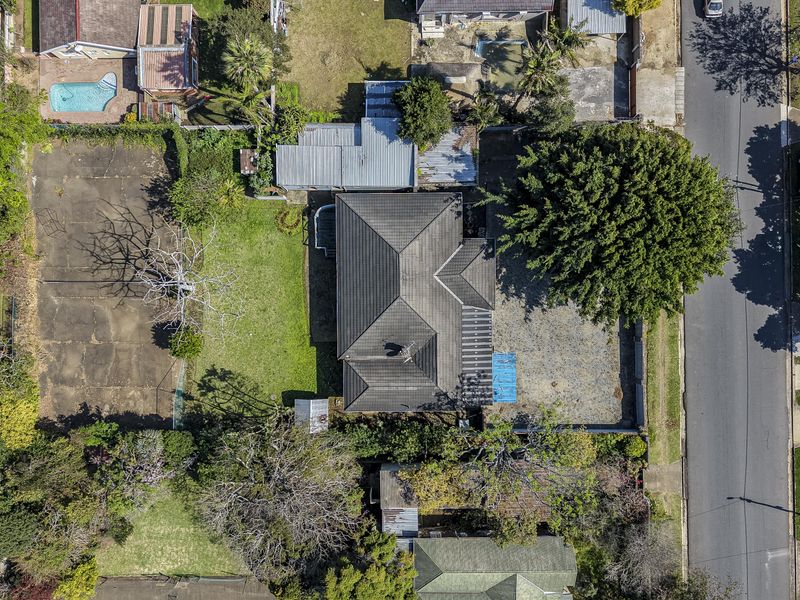 Aerial view of the property showing the main dwelling, large garden area, paved driveway, and surrounding residential neighborhood context.