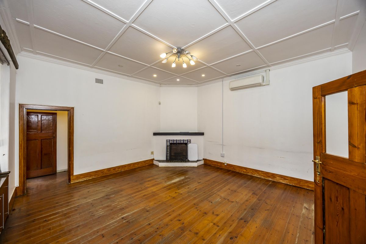 Spacious living room featuring original hardwood flooring, a corner fireplace, and a decorative coffered ceiling, offering a blank canvas for interior design.