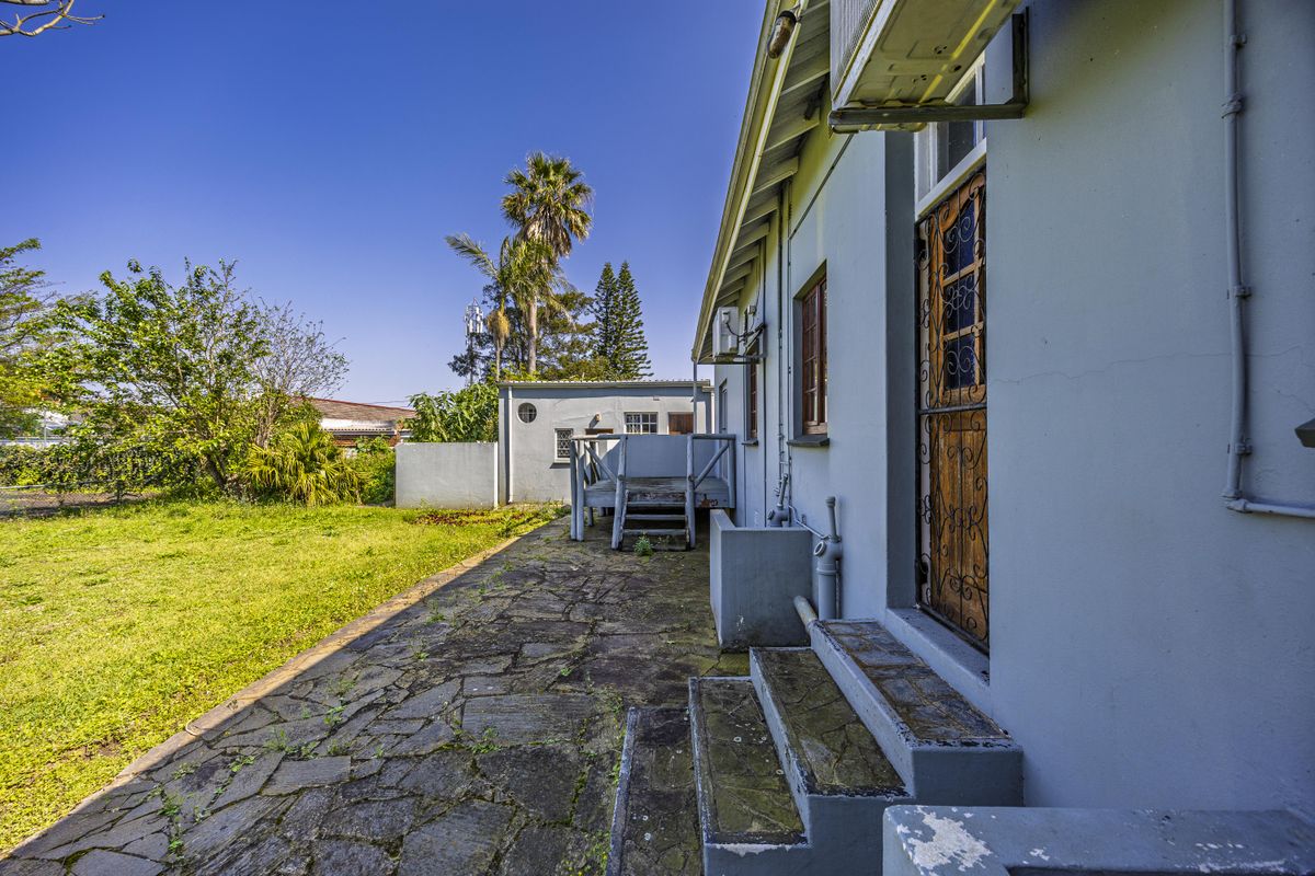 Rear exterior view featuring a stone paved patio, concrete steps, and a detached outbuilding set within a garden area.