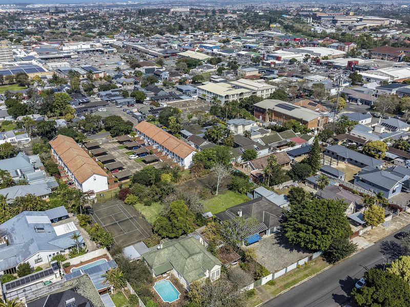 An aerial view of a residential neighborhood featuring houses with tiled roofs, a private swimming pool, and a tennis court.