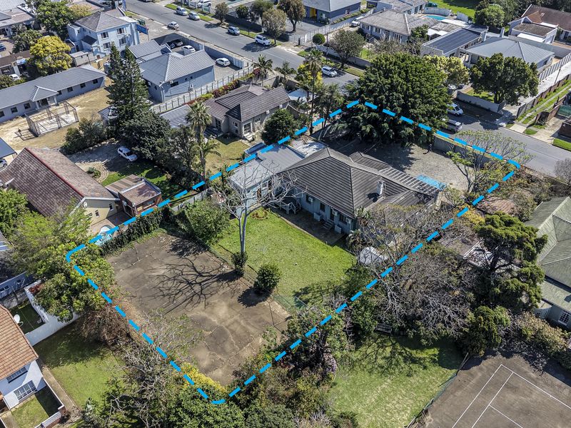 Aerial view of a residential property featuring a large garden, tiled roof structure, and paved driveway area within a suburban neighborhood setting.