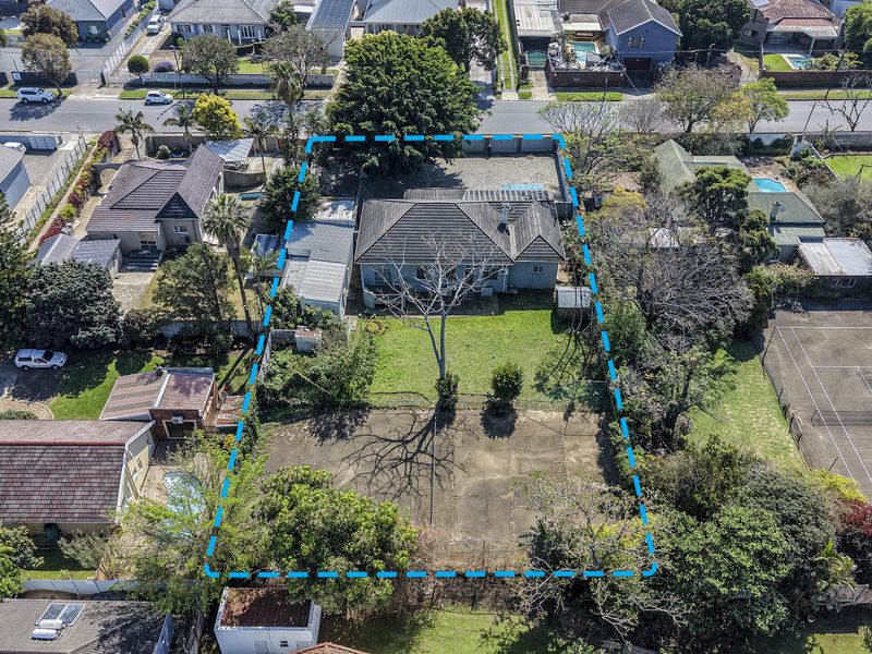 Aerial view of the property highlighting the residential dwelling, expansive garden, paved driveway, and concrete court area within the fenced boundary.