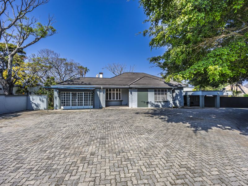 Front view of the property featuring a spacious paved driveway, covered entrance, and secure boundary walls, providing ample parking space.