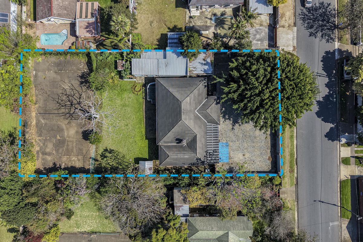 Aerial view of the property showing the main dwelling, large lawn area, paved sections, and surrounding boundary lines.