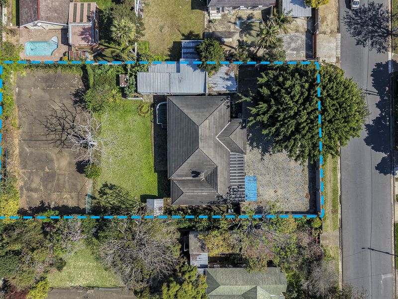 Aerial view of the property showing the main dwelling, large lawn area, paved sections, and surrounding boundary lines.