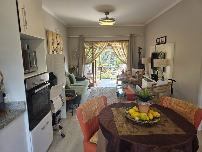 Open-plan living and dining area featuring a compact kitchen with built-in appliances, leading directly to a private patio through sliding glass doors.