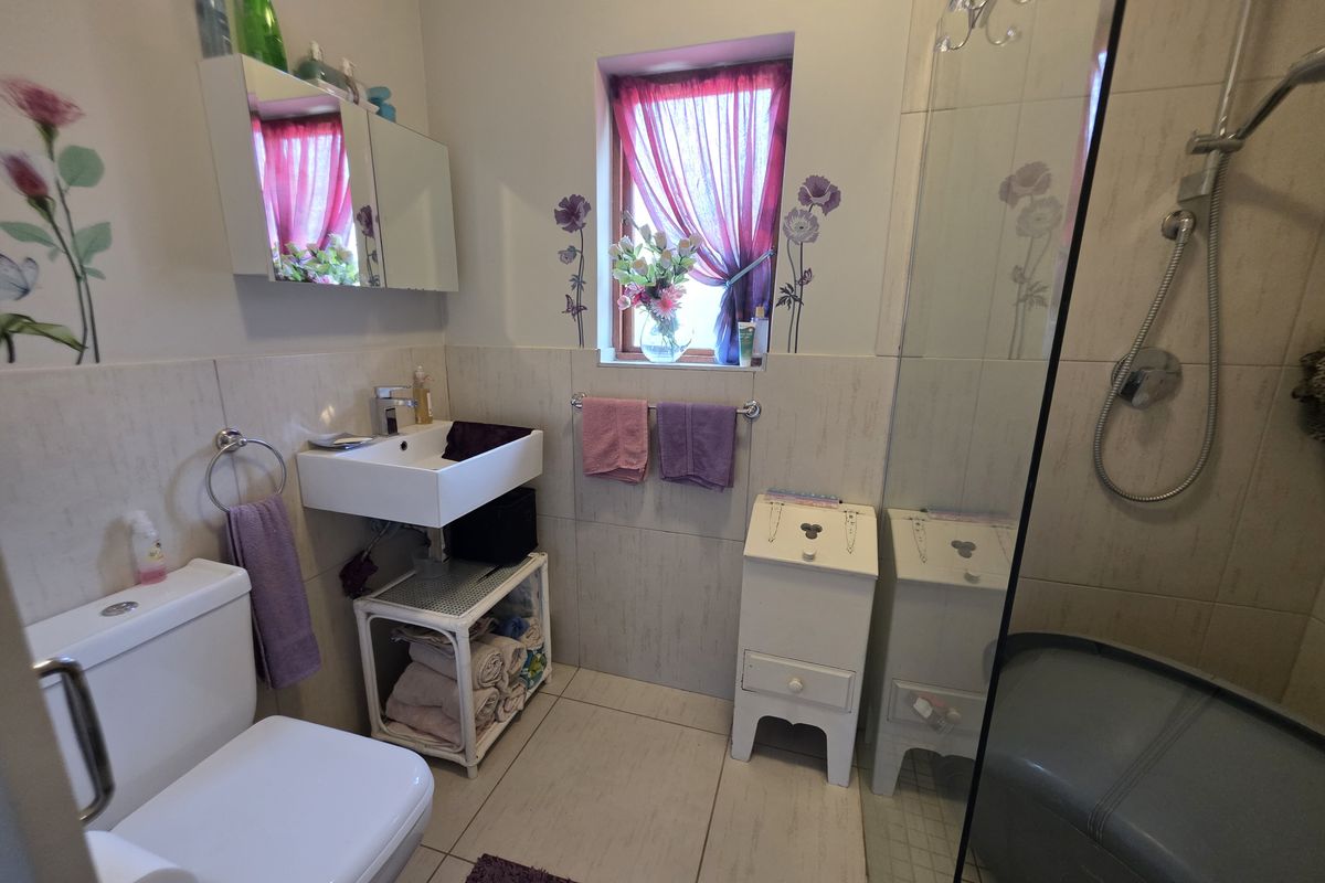 A functional bathroom featuring a wall-mounted basin, a shower enclosure, and tiled finishes, providing a clean and practical space.