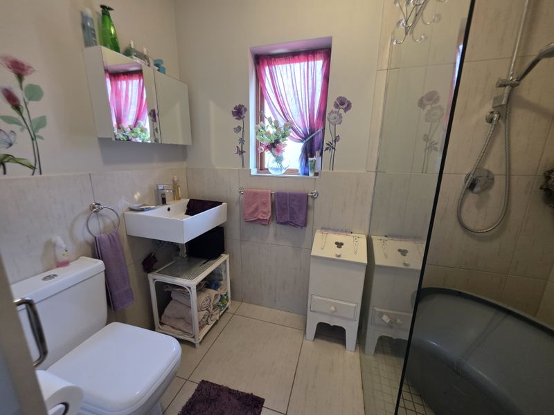 A functional bathroom featuring a wall-mounted basin, a shower enclosure, and tiled finishes, providing a clean and practical space.