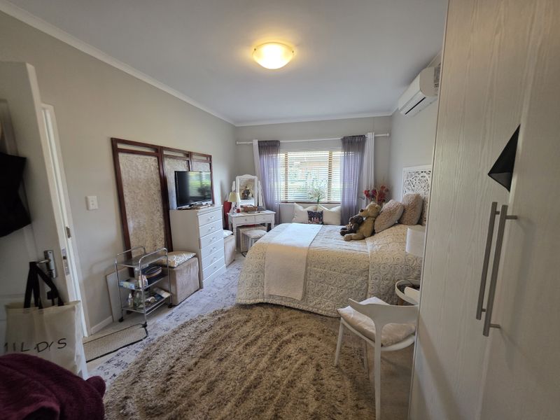 A well-maintained bedroom featuring a built-in wardrobe, split-system air conditioning, and natural light through window blinds.