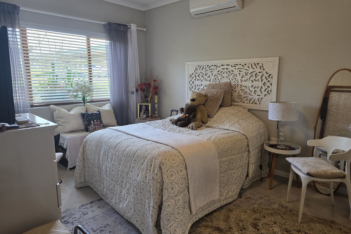 A comfortable bedroom featuring a wall-mounted split-system air conditioner and venetian blinds, providing a functional and climate-controlled living space.