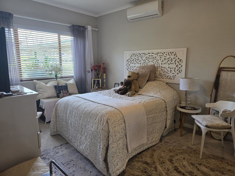 A comfortable bedroom featuring a wall-mounted split-system air conditioner and venetian blinds, providing a functional and climate-controlled living space.