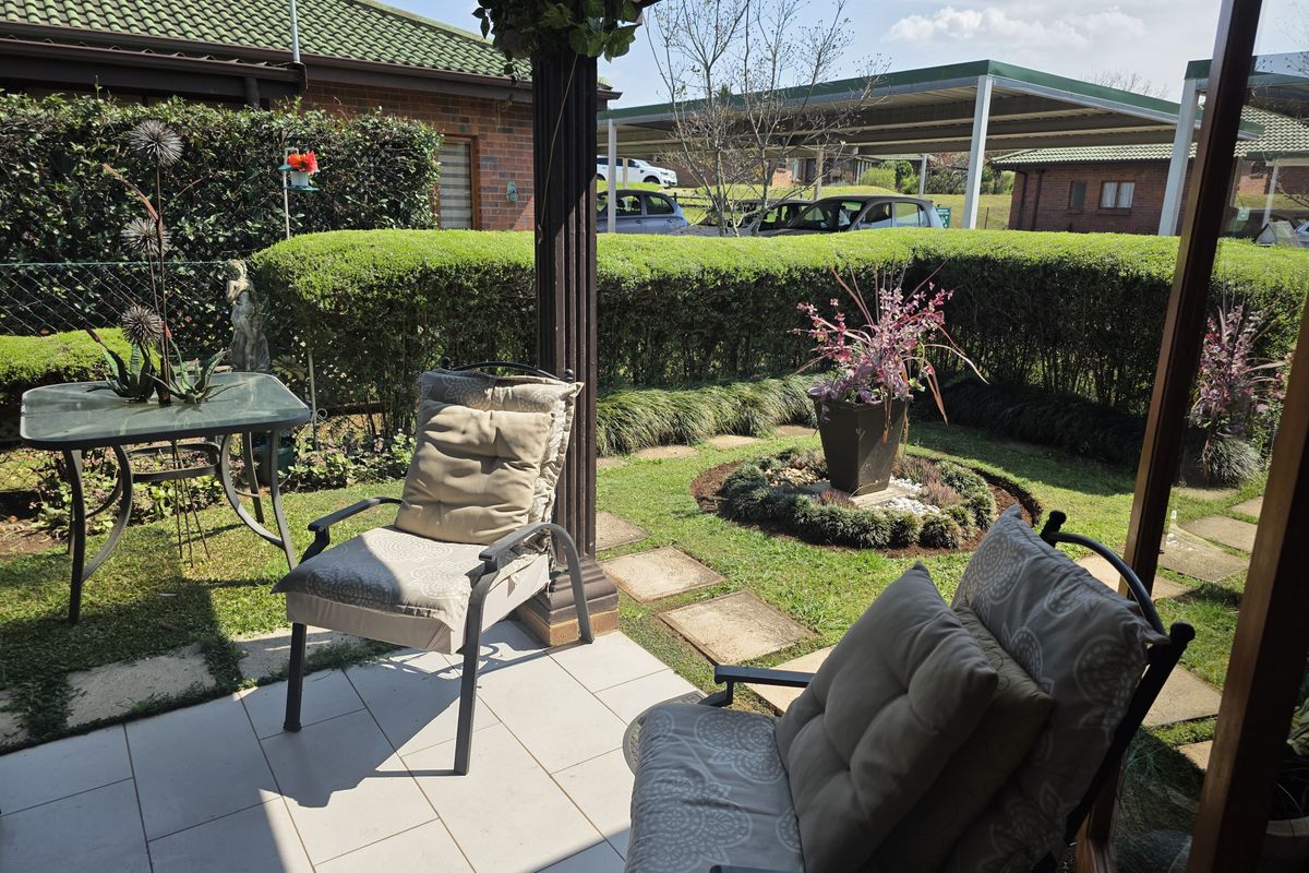 A well-maintained covered patio area featuring tiled flooring, overlooking a neatly landscaped private garden with established hedging and stone pathways.