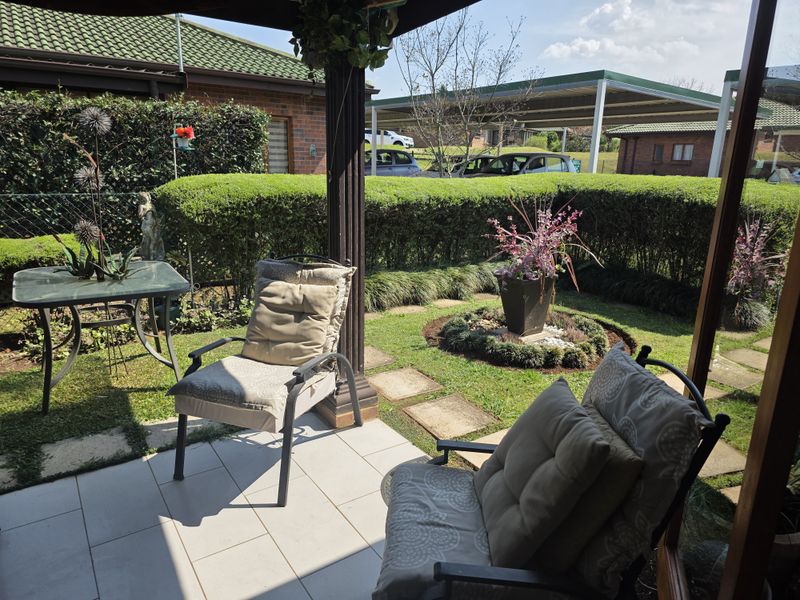 A well-maintained covered patio area featuring tiled flooring, overlooking a neatly landscaped private garden with established hedging and stone pathways.