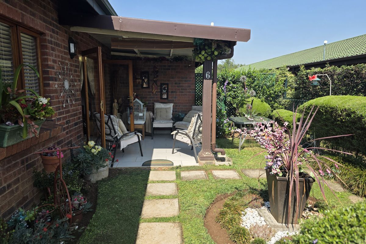 A well-maintained covered patio area featuring brick exterior walls, tiled flooring, and direct access to a landscaped garden space.