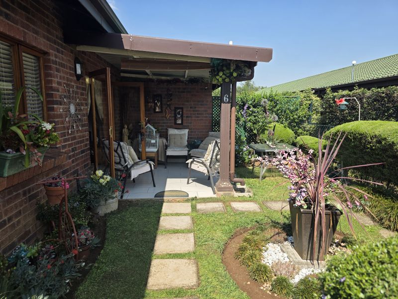 A well-maintained covered patio area featuring brick exterior walls, tiled flooring, and direct access to a landscaped garden space.