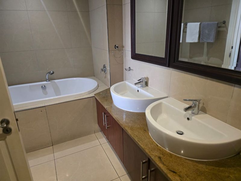 A well-maintained bathroom featuring a double vanity with granite countertops, under-counter cabinetry, and a built-in bathtub with neutral wall and floor tiling.