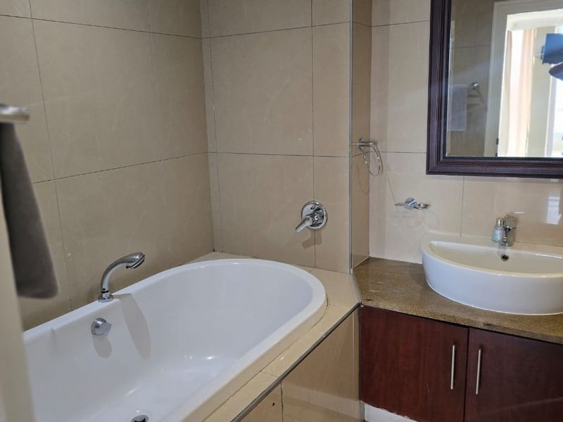 A clean, modern bathroom featuring a built-in bathtub, a vanity cabinet with a countertop basin, and neutral wall tiling.