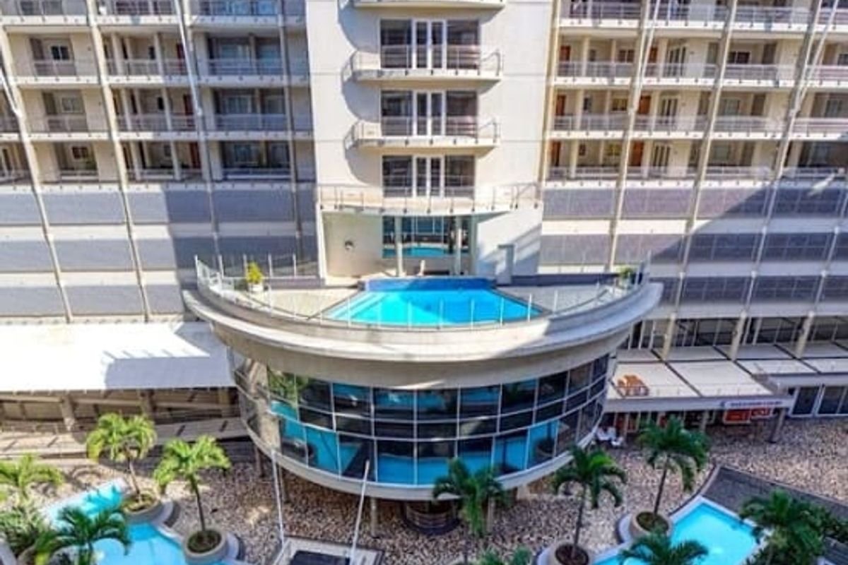 Aerial view of the apartment complex featuring a central swimming pool, landscaped garden areas, and multiple levels of private balconies with glass railings.