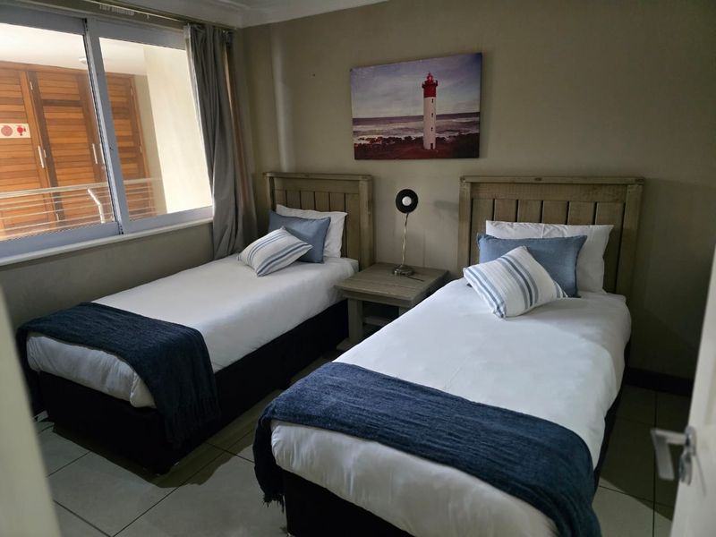 A well-maintained bedroom featuring tiled flooring and a large sliding window, providing natural light and a view of the adjacent balcony area.