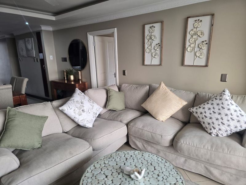 A comfortable living room featuring crown molding, recessed ceiling details, and neutral tiled flooring, providing a well-maintained and inviting space.
