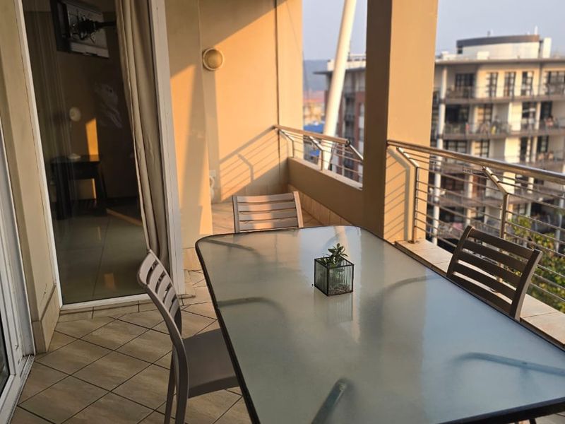 A covered balcony featuring tiled flooring and a stainless steel balustrade, offering an outdoor space accessible via a sliding glass door.