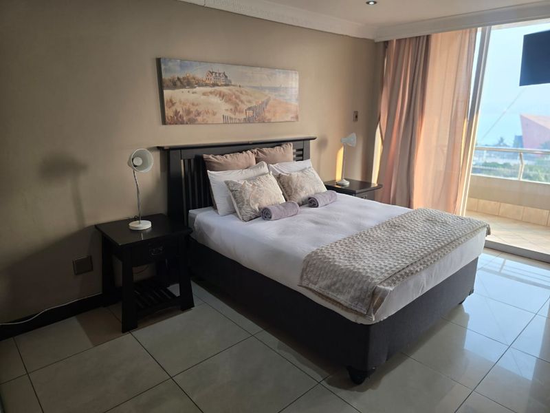 A well-maintained bedroom featuring tiled flooring, crown molding, and a sliding glass door providing access to a balcony with exterior views.