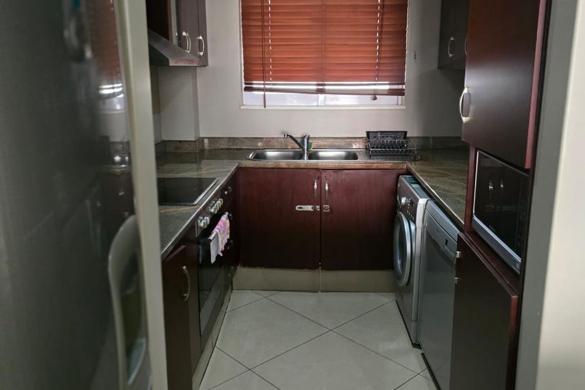 A compact, functional kitchen featuring dark wood cabinetry, tiled flooring, integrated appliances, and a window with venetian blinds.
