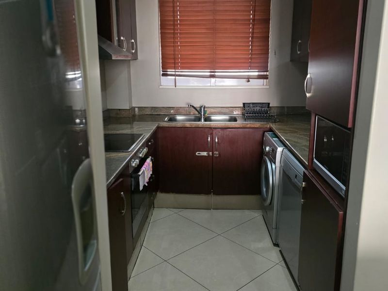 A compact, functional kitchen featuring dark wood cabinetry, tiled flooring, integrated appliances, and a window with venetian blinds.
