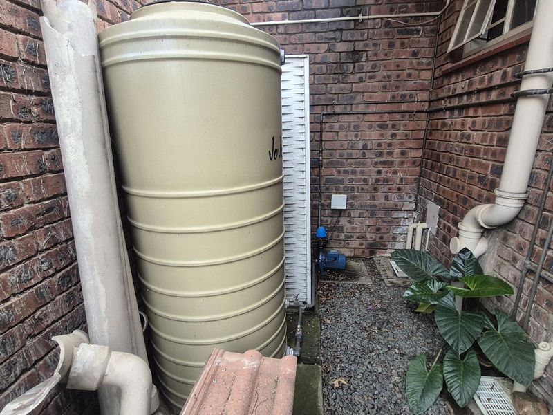 Utility area featuring a water storage tank and pump system installed against a brick exterior wall.