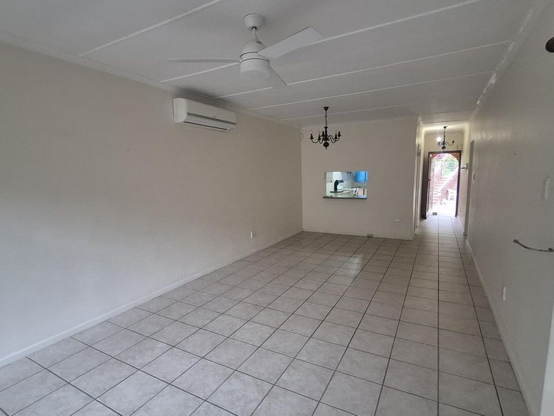 Spacious open-plan living area featuring ceramic floor tiles, a ceiling fan, and a split-system air conditioner, with a serving hatch connecting to the kitchen.