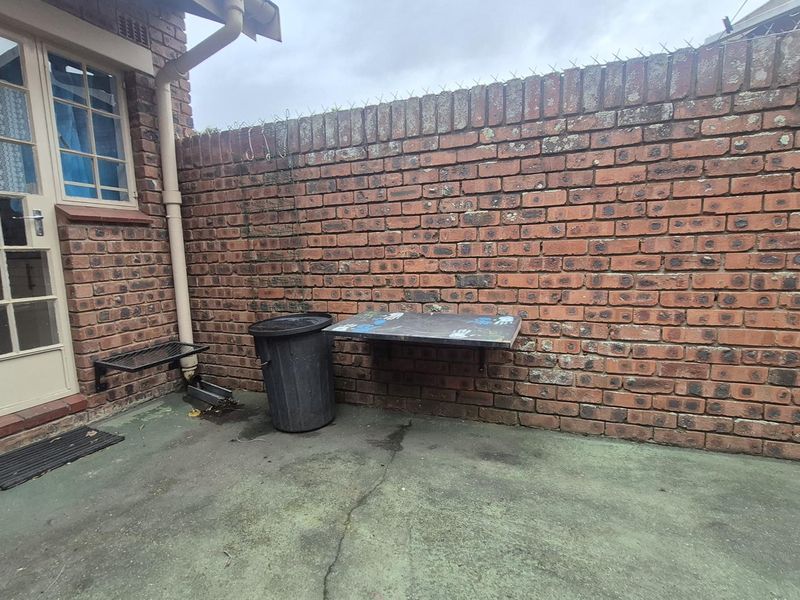 A rear courtyard area featuring a brick boundary wall, concrete paving, and direct access to the townhouse via a french door.