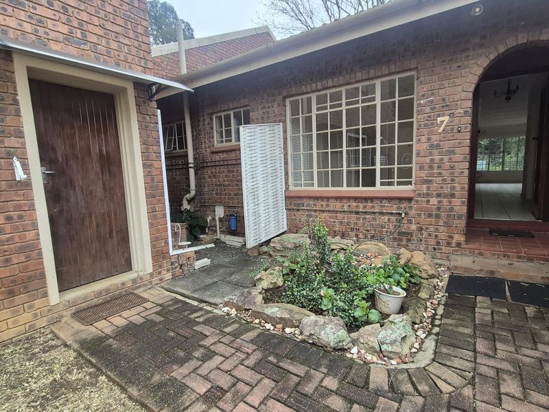 Front entrance area of a facebrick townhouse featuring a paved courtyard, rockery garden, and arched doorway.