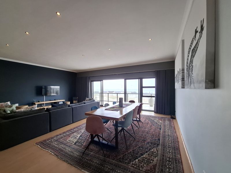 Spacious open-plan living and dining area featuring modern recessed lighting, laminate flooring, and large sliding doors leading to a balcony with coastal views.