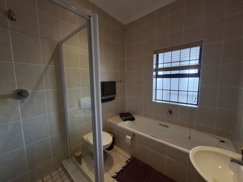A functional bathroom featuring a tiled shower enclosure, a built-in bathtub, a wall-mounted toilet, and a basin with neutral wall tiling.