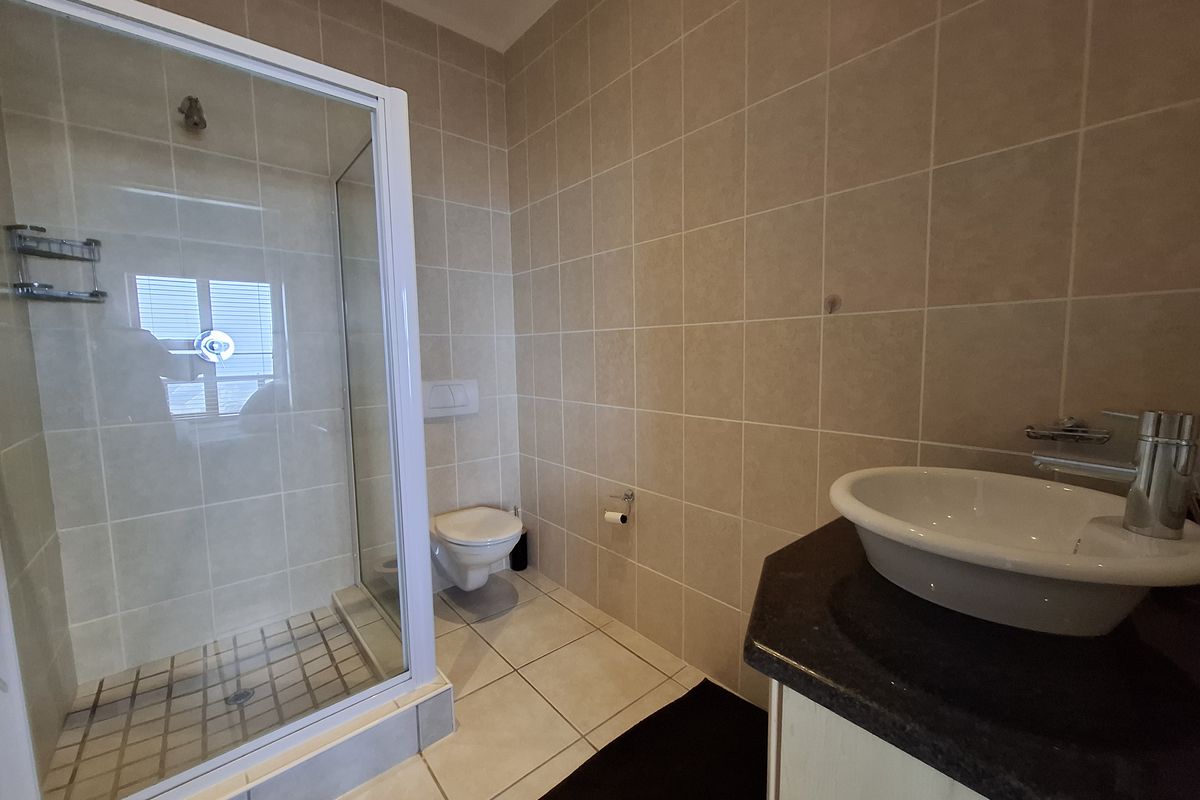 A clean, functional bathroom featuring a glass shower enclosure, wall-mounted toilet, and a modern vanity basin with a dark countertop.