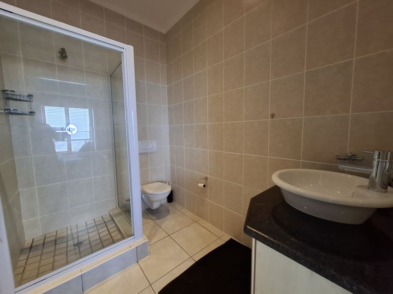 A clean, functional bathroom featuring a glass shower enclosure, wall-mounted toilet, and a modern vanity basin with a dark countertop.