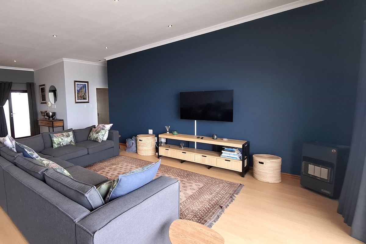 Spacious living room featuring laminate flooring, recessed downlighting, and a feature wall with a mounted television and gas heater.