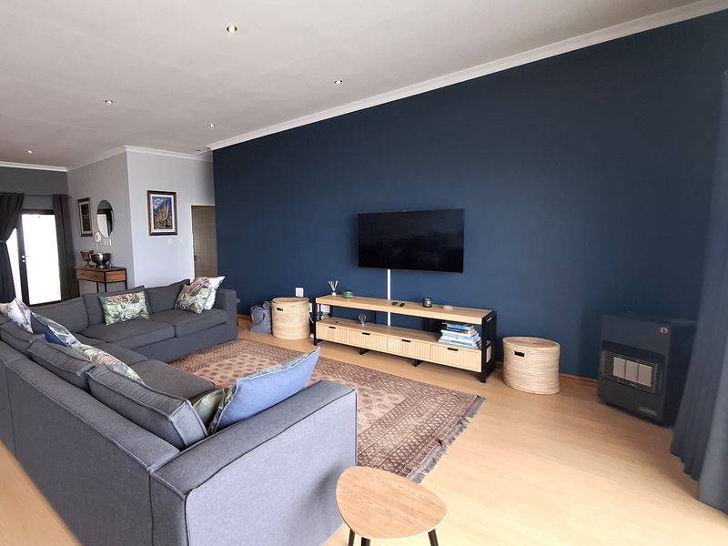 Spacious living room featuring laminate flooring, recessed downlighting, and a feature wall with a mounted television and gas heater.