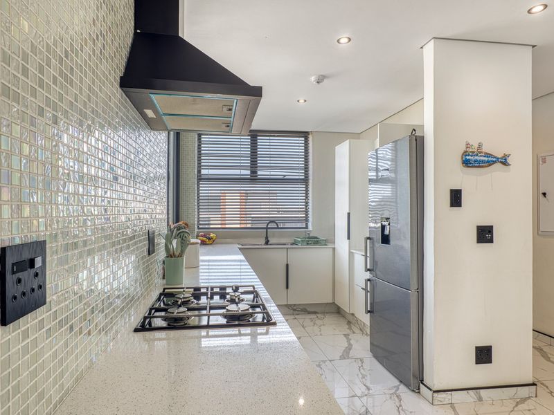 Modern kitchen featuring a mosaic tile backsplash, quartz countertops, gas hob with extractor, and sleek white cabinetry with marble-look floor tiles.