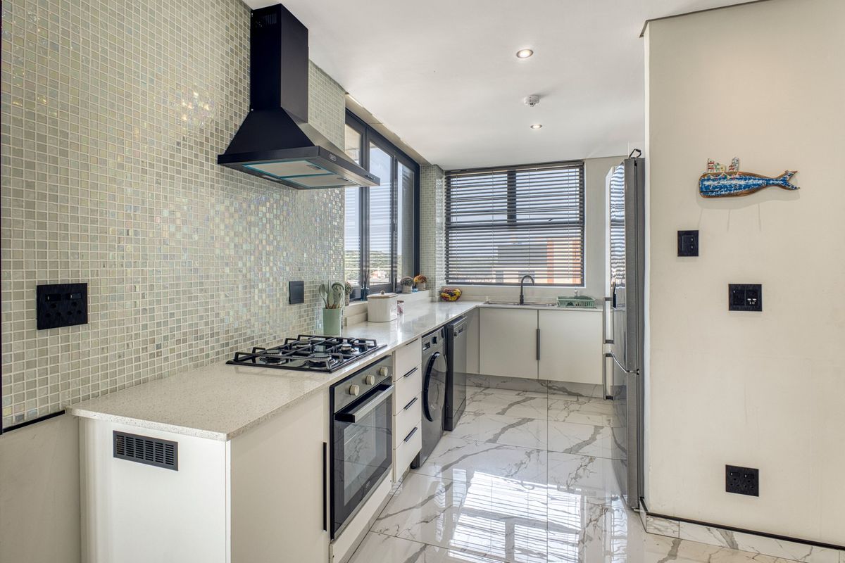 Modern kitchen featuring a mosaic tile backsplash, stone countertops, gas hob, built-in oven, and elegant marble-look floor tiles with ample natural light.