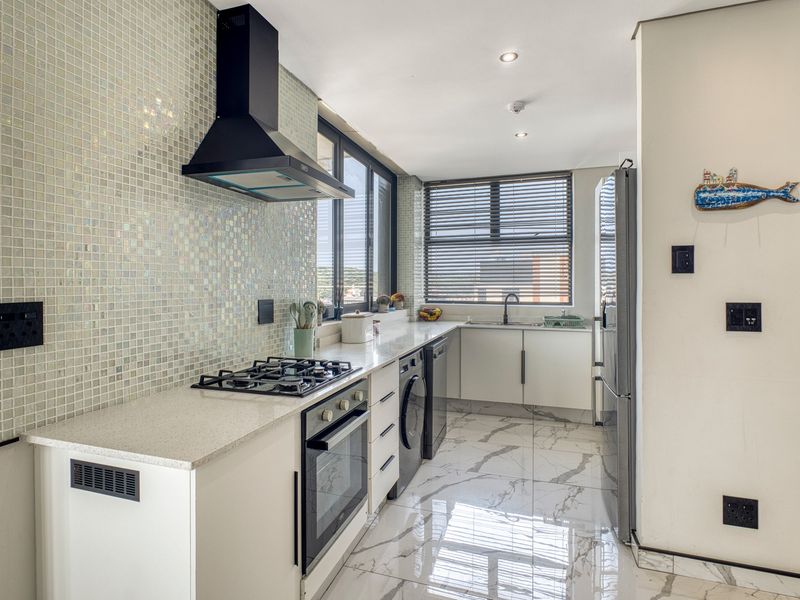 Modern kitchen featuring a mosaic tile backsplash, stone countertops, gas hob, built-in oven, and elegant marble-look floor tiles with ample natural light.