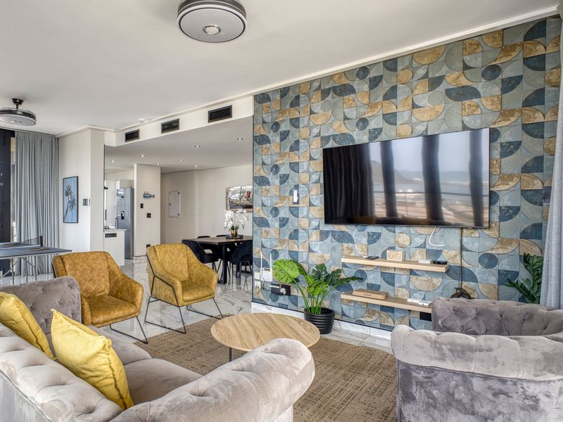 Modern open-plan living area featuring a striking geometric feature wall, marble-look flooring, recessed lighting, and seamless access to the balcony.