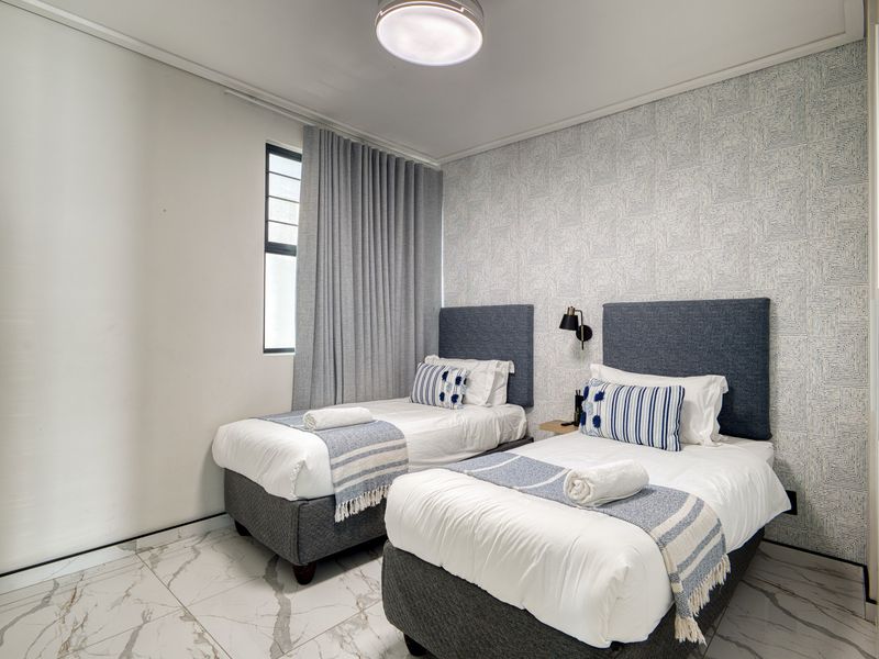 A well-maintained bedroom featuring marble-look floor tiles, textured accent wallpaper, and modern wall-mounted lighting.