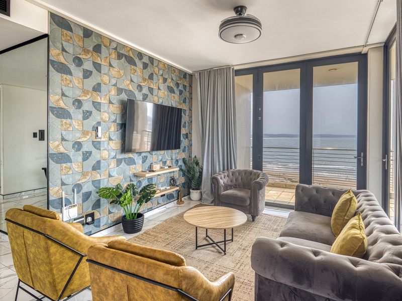 Modern living room featuring a striking patterned feature wall, marble-look flooring, and large glass doors opening to a balcony with ocean views.