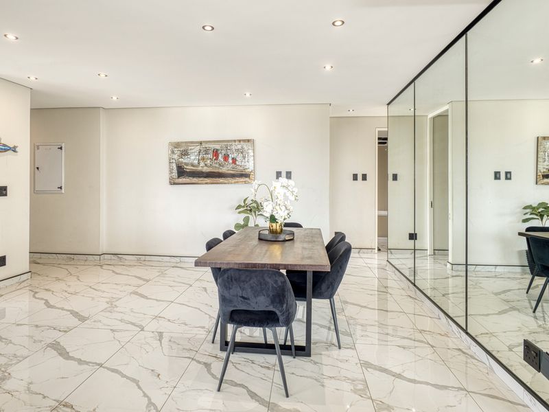 Modern dining area featuring polished marble-look floor tiles, recessed ceiling lighting, and a large mirrored wall feature that enhances the sense of space.