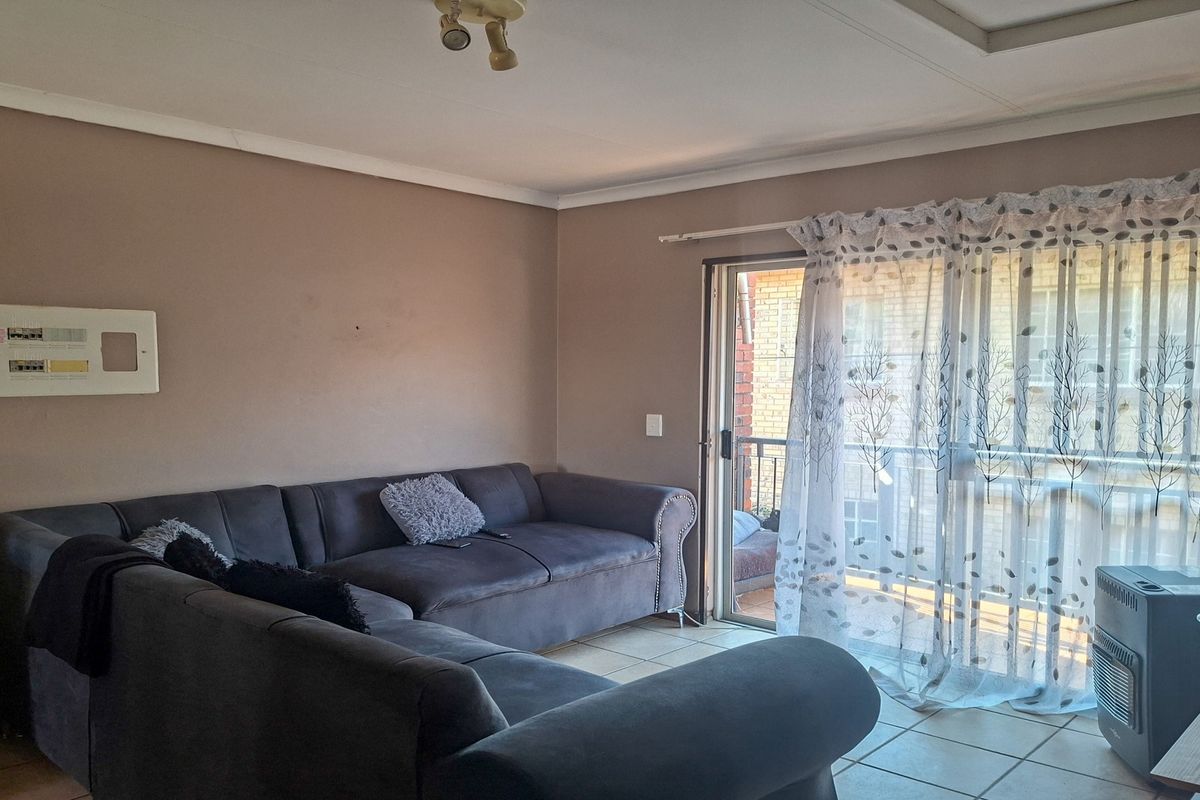 A living room featuring tiled flooring, a sliding glass door leading to a balcony, and a wall-mounted electrical distribution board.