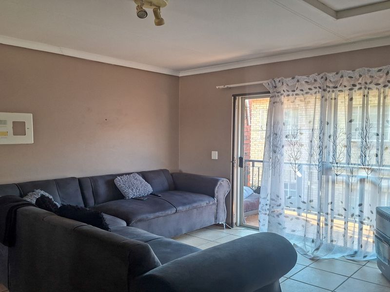 A living room featuring tiled flooring, a sliding glass door leading to a balcony, and a wall-mounted electrical distribution board.