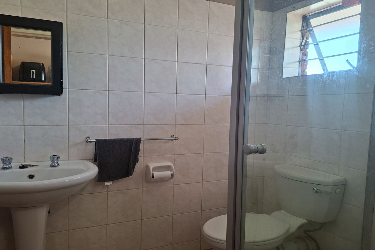 A functional bathroom featuring a pedestal basin, toilet, and a glass-enclosed shower with tiled walls and a small window for natural light.