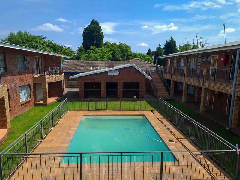 Communal apartment complex courtyard featuring a swimming pool, paved surround, and brick building facades with balconies and stair access.